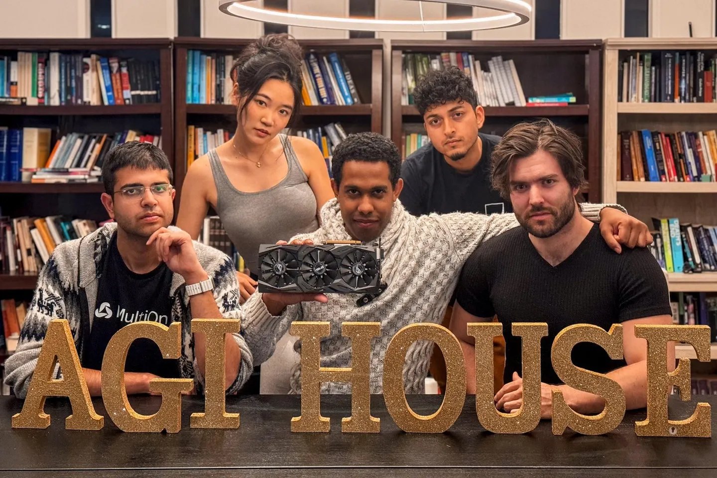 Hackathon winners at AGI House holding their GPU prize behind gold AGI House letters